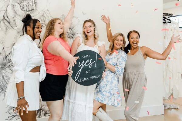 A bride holding a "I said yes at Leora Bridal" sign together with her bridal party
