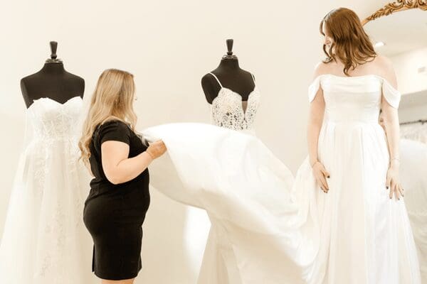A bride trying on her wedding gown while her stylist fixes her train