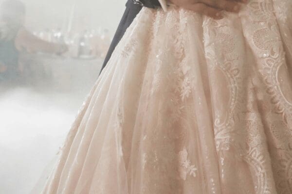 Close-up of a couple dancing; the focus is on the bride's lace, embroidered wedding dress. Soft lighting creates a romantic, dreamy atmosphere.