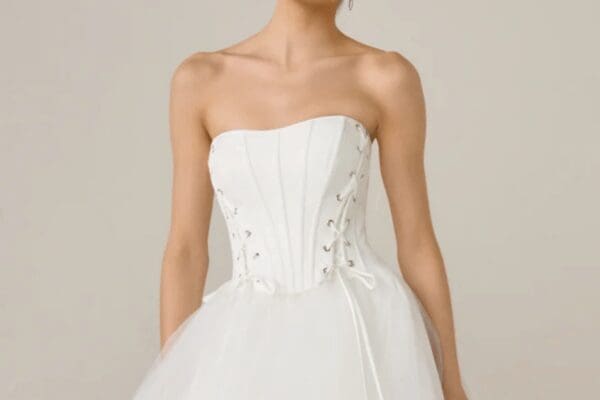 Strapless white wedding dress with a fitted corset top featuring lace-up detailing, leading to a full tulle skirt. Elegant and romantic tone.