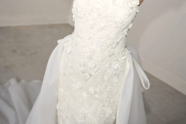 Elegant white wedding dress with floral lace appliqué, a fitted bodice, and flowing tulle skirt. Soft lighting creates a romantic, delicate atmosphere.
