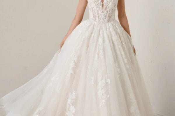 A bride wears a white lace wedding dress with a deep V-neck and a voluminous skirt, exuding elegance and romance against a plain background.