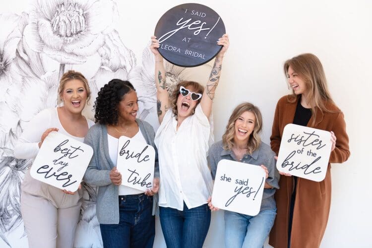 Bride celebrating with friends holding “I said yes” and bridal signs after choosing her wedding dress at Leora Bridal.