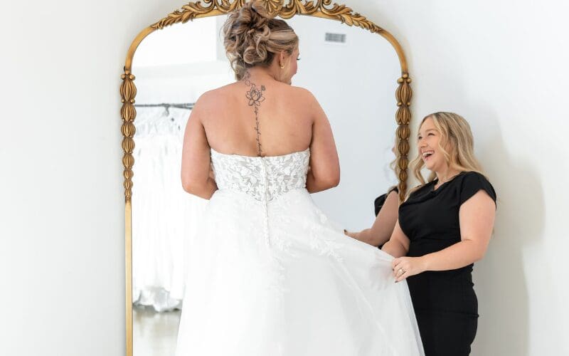 Bride trying on a strapless wedding dress with a stylist adjusting the gown in a boutique
