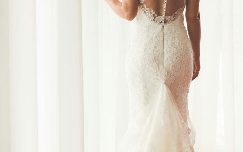 Close-up back view of a bride wearing a fitted lace wedding dress with a sheer open back and flowing train.
