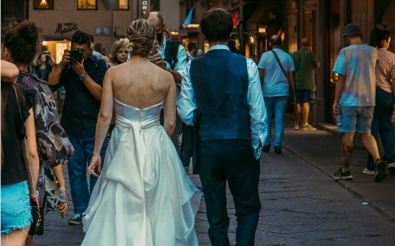 Bride and groom walking through a city street while the bride wears a satin wedding gown with a softly bustled train gathered at the back.