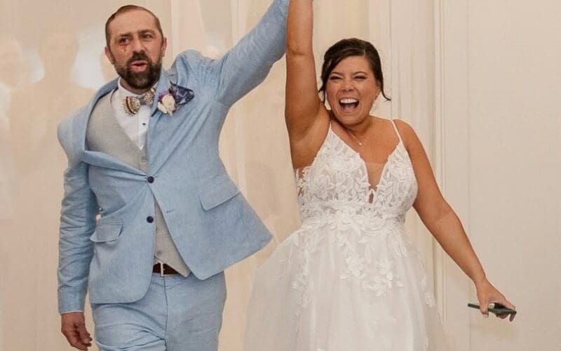 Bride and groom celebrate their wedding reception entrance with raised arms and big smiles.
