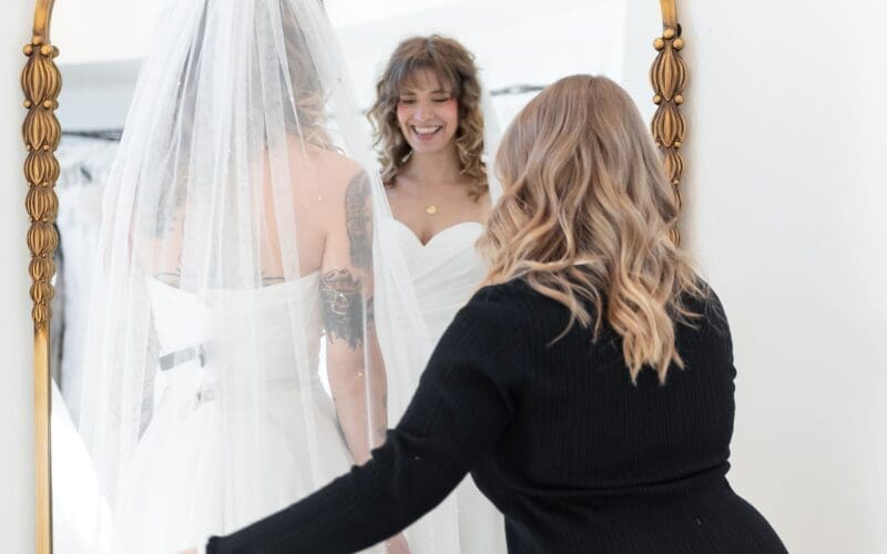 Bride trying on a wedding veil while meeting with a bridal stylist during her first wedding dress fitting.