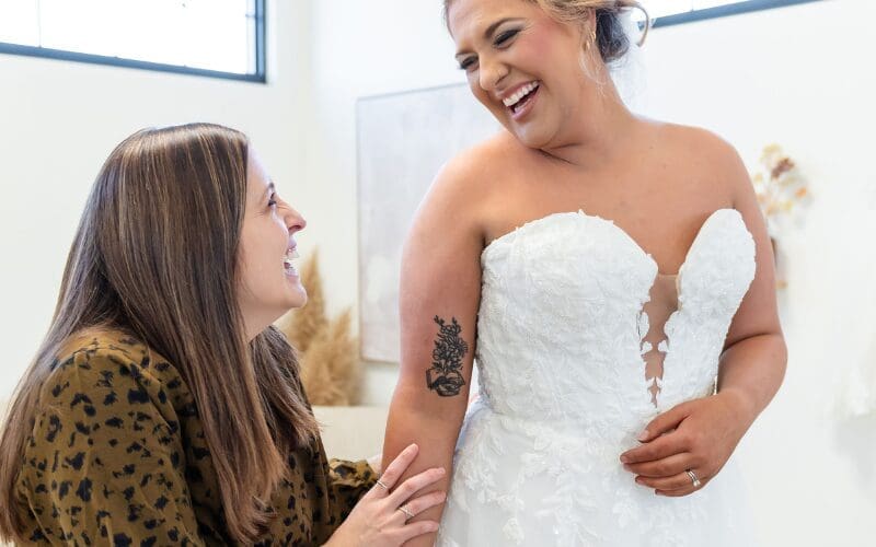 Bride trying on a wedding dress while consulting with a bridal stylist during a fitting appointment.