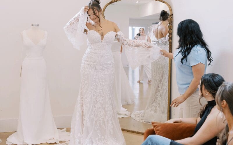 Bride trying on a lace wedding dress with bridal stylist in boutique