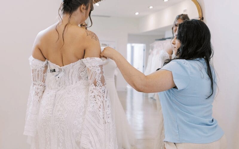 Bridal stylist adjusting the back of a lace wedding dress during fitting