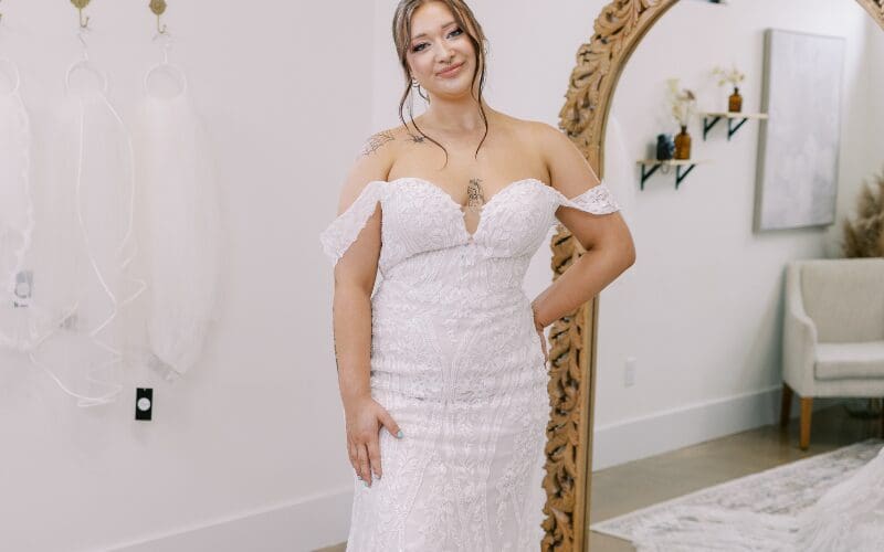 Bride wearing a lace off-the-shoulder wedding dress in a bridal boutique