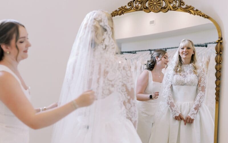 Bride trying on a lace wedding dress with her bridal stylist in a boutique