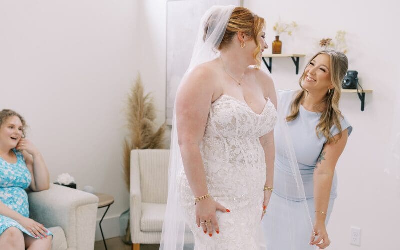 Bride admiring a fitted lace wedding dress with her bridal stylist